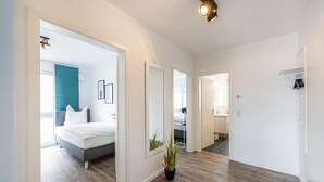 A modern hotel room with a bed, a potted plant, and a hallway leading to a bathroom. - Lovely apartment in Rechlin with lake view (Rechlin)