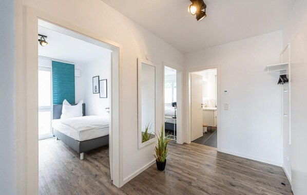 Una habitación de hotel moderna con una cama, una planta en maceta y un pasillo que conduce a un baño.