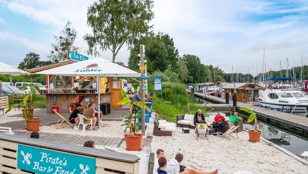 A beachside bar with outdoor seating and a view of boats on the water. - Lovely apartment in Rechlin with lake view (Rechlin)