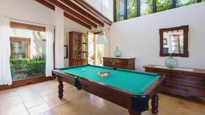 Una mesa de billar en una habitación con vigas de madera, un armario y un espejo en la pared.