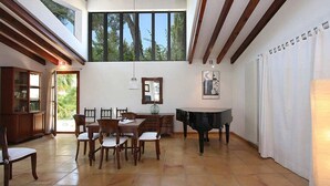 Un comedor con piano, sillas de madera, una mesa y un ventanal con vistas a árboles.