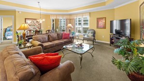 A living room with a brown leather sofa, a glass coffee table, a television, and a large potted plant. - Royale Palms 704 2 Br Oceanview in Kingston, Pool (Myrtle Beach)