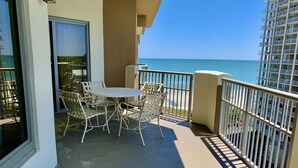 A balcony with a table and chairs, overlooking a clear blue sea. - Royale Palms 704 2 Br Oceanview in Kingston, Pool (Myrtle Beach)