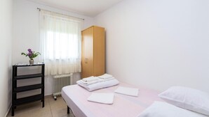 Une chambre à coucher avec un lit, une armoire en bois, un radiateur, une étagère noire et une fenêtre avec des rideaux légers.