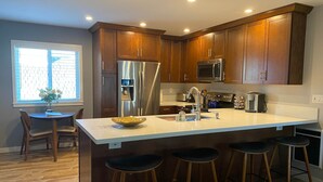 Une cuisine moderne avec des meubles en bois, des appareils en acier inoxydable, un grand îlot central avec des tabourets et une fenêtre qui laisse entrer la lumière naturelle.
