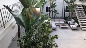 Une terrasse extérieure couverte, dotée d’un espace salon, de grandes plantes et d’un escalier.