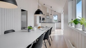 Une cuisine moderne avec des meubles blancs, un îlot central, des luminaires suspendus et une vue sur l’extérieur.