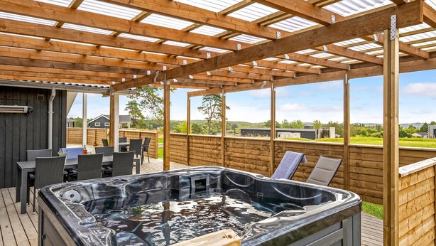 Une terrasse en bois avec un jacuzzi, du mobilier d’extérieur et une vue sur les environs.