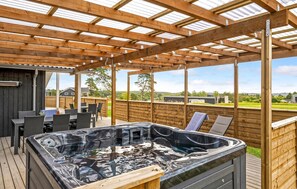 Une terrasse en bois avec un jacuzzi, du mobilier d’extérieur et une vue sur les environs.
