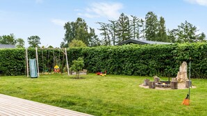 A backyard with a wooden deck, a swing set, a slide, and a fire pit. - Nice home in Kirke Hyllinge with WiFi (Kirke Hyllinge)