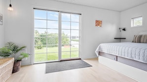 A bedroom with a large sliding glass door to a garden, a bed with a white quilt, a bedside table, a lamp, and a framed picture on the wall. - Nice home in Kirke Hyllinge with WiFi (Kirke Hyllinge)