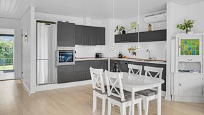 A modern kitchen with a built-in oven, a dining area with white chairs, and a view of the outdoors through a large window. - Nice home in Kirke Hyllinge with WiFi (Kirke Hyllinge)