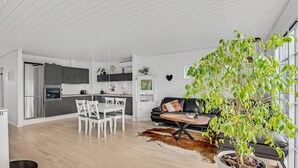 A modern kitchen with stainless steel appliances, a dining area with white chairs, and a living room with a leather sofa and a large potted plant. - Nice home in Kirke Hyllinge with WiFi (Kirke Hyllinge)
