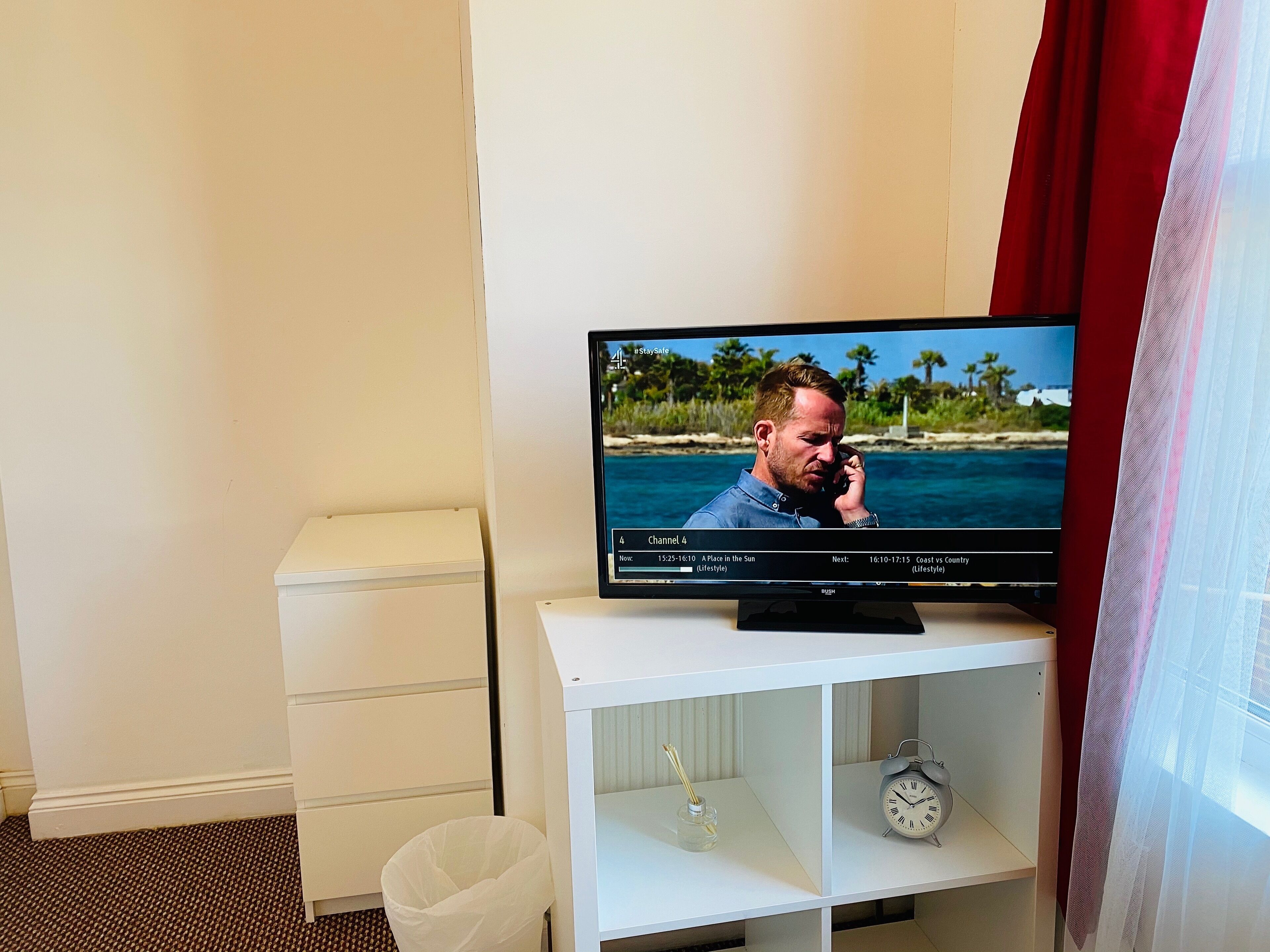A television on a white stand displaying a man on a beach.