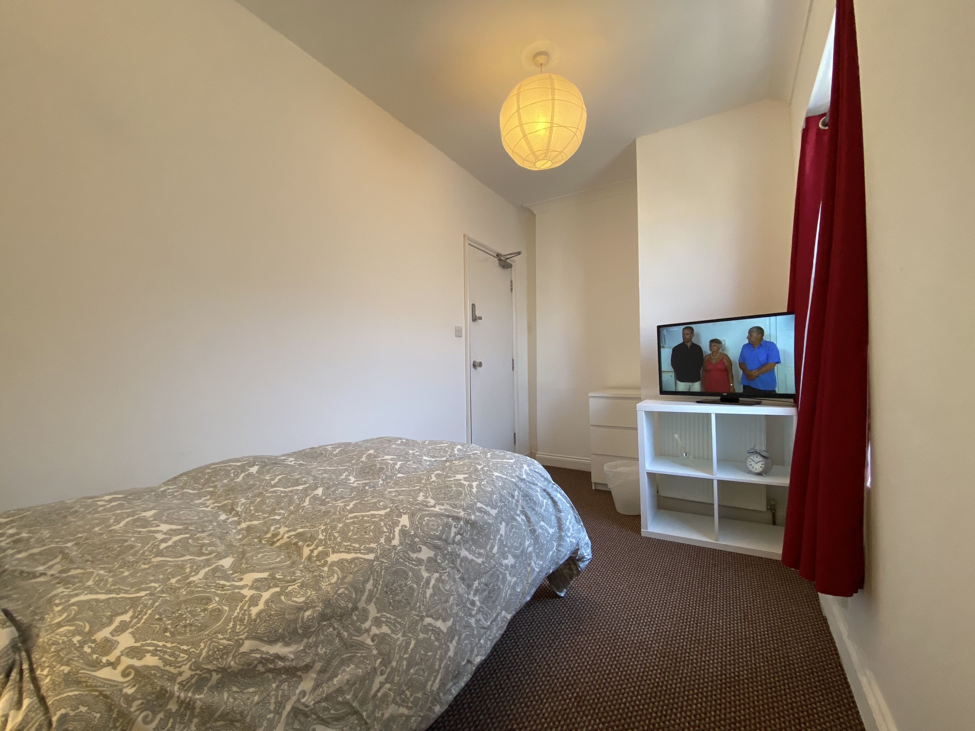 A bedroom with a bed, a television, a wardrobe, and a hanging light fixture.