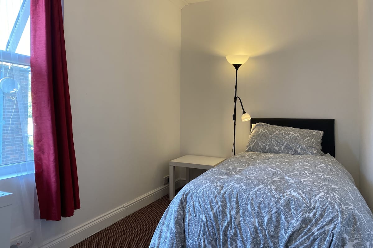 A bedroom with a bed, a nightstand, a floor lamp, and a window with curtains.