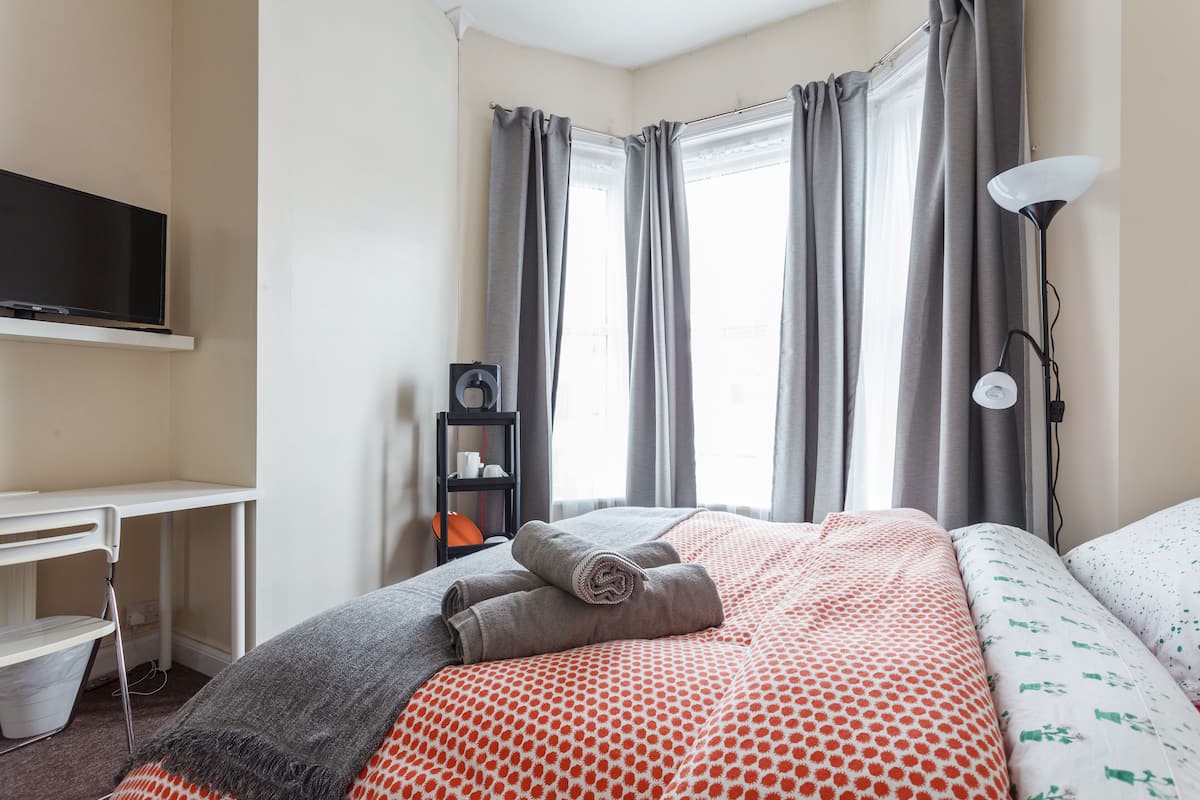 A hotel room with a bed, a desk, a TV, and a window with curtains.