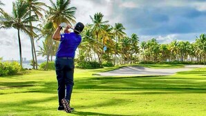 A golfer on a golf course with palm trees and a clear sky.