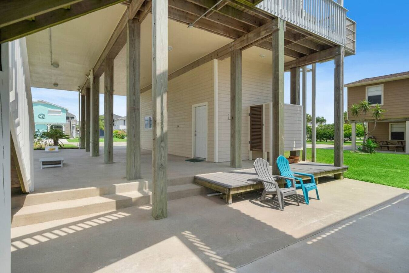 A covered outdoor area with wooden columns, a concrete floor, and a seating area with two chairs.