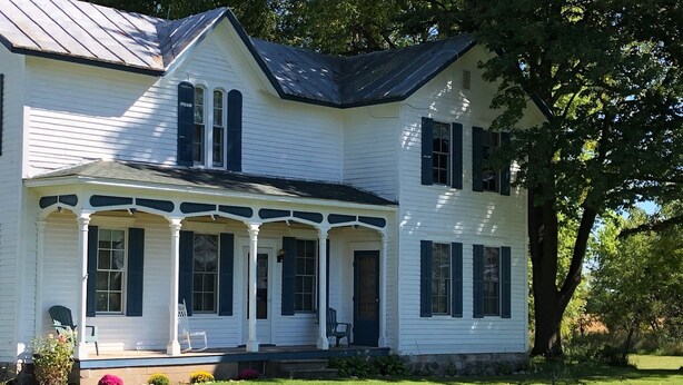 A two-story white house with dark shutters, a porch with chairs, and a well-maintained lawn. - Have a Summer Holiday in Country Farmhouse (Schoolcraft)