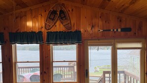 A cabin with wooden walls and a large window overlooking a lake. - Waterfront Camp with Boathouse - Wifi, kayaks, canoe and sandy bottom out front. (Old Forge)