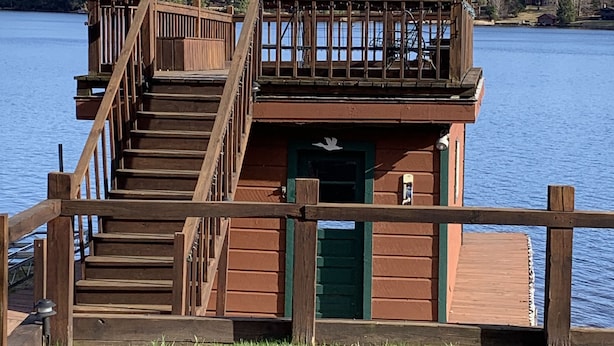 A wooden dock with a staircase leading to a cabin with a green door, surrounded by water and trees. - Waterfront Camp with Boathouse - Wifi, kayaks, canoe and sandy bottom out front. (Old Forge)