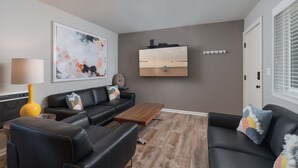Un salon moderne avec un canapé en cuir noir, une table basse en bois et un téléviseur à écran plat fixé au mur.