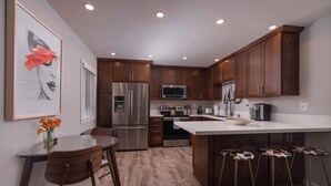 Une cuisine moderne avec des meubles en bois, des appareils en acier inoxydable, un îlot central doté de tabourets et un coin repas avec une table et des chaises en verre.