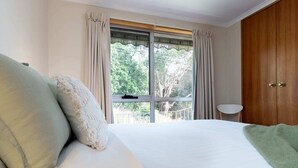 A bedroom with a large bed, a view through a window, and a wooden wardrobe.