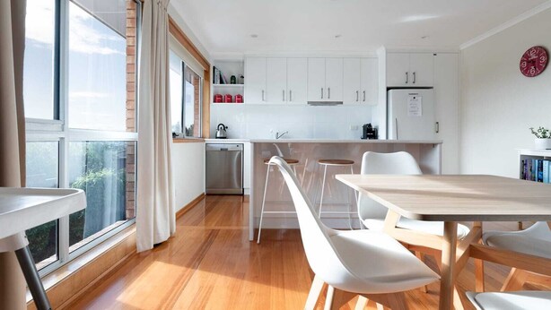 A modern kitchen with white cabinets, a wooden dining table, and white chairs.