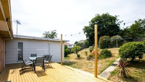 A wooden deck with a table and chairs, a small building with a door, and a garden with trees and shrubs. - Family Escape | Views & Wi-Fi (Newstead)