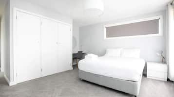 A modern bedroom with a large bed, a desk, and a wardrobe.