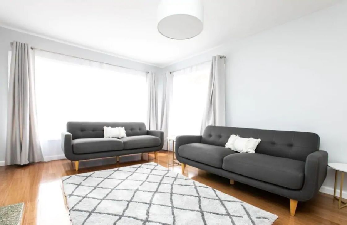 A modern living room with two dark sofas, a white rug, and a ceiling light.
