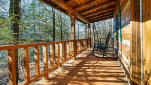 Une terrasse en bois avec une balustrade, une chaise berçante et une vue sur une forêt.