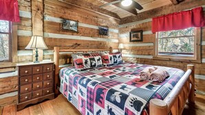 Une chambre située dans un chalet en rondins, avec un lit en bois, une table de chevet, une commode et un ventilateur de plafond.
