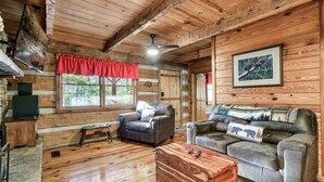 L’intérieur d’un chalet accueillant, avec des murs en bois, une cheminée, deux canapés en cuir, une table basse en bois et un téléviseur.