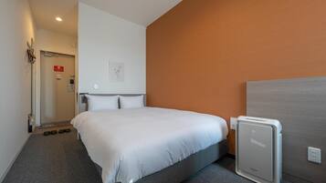 Une chambre d’hôtel comprenant un lit, une table de chevet, un radiateur fixé au mur et une porte donnant accès à la salle de bain.