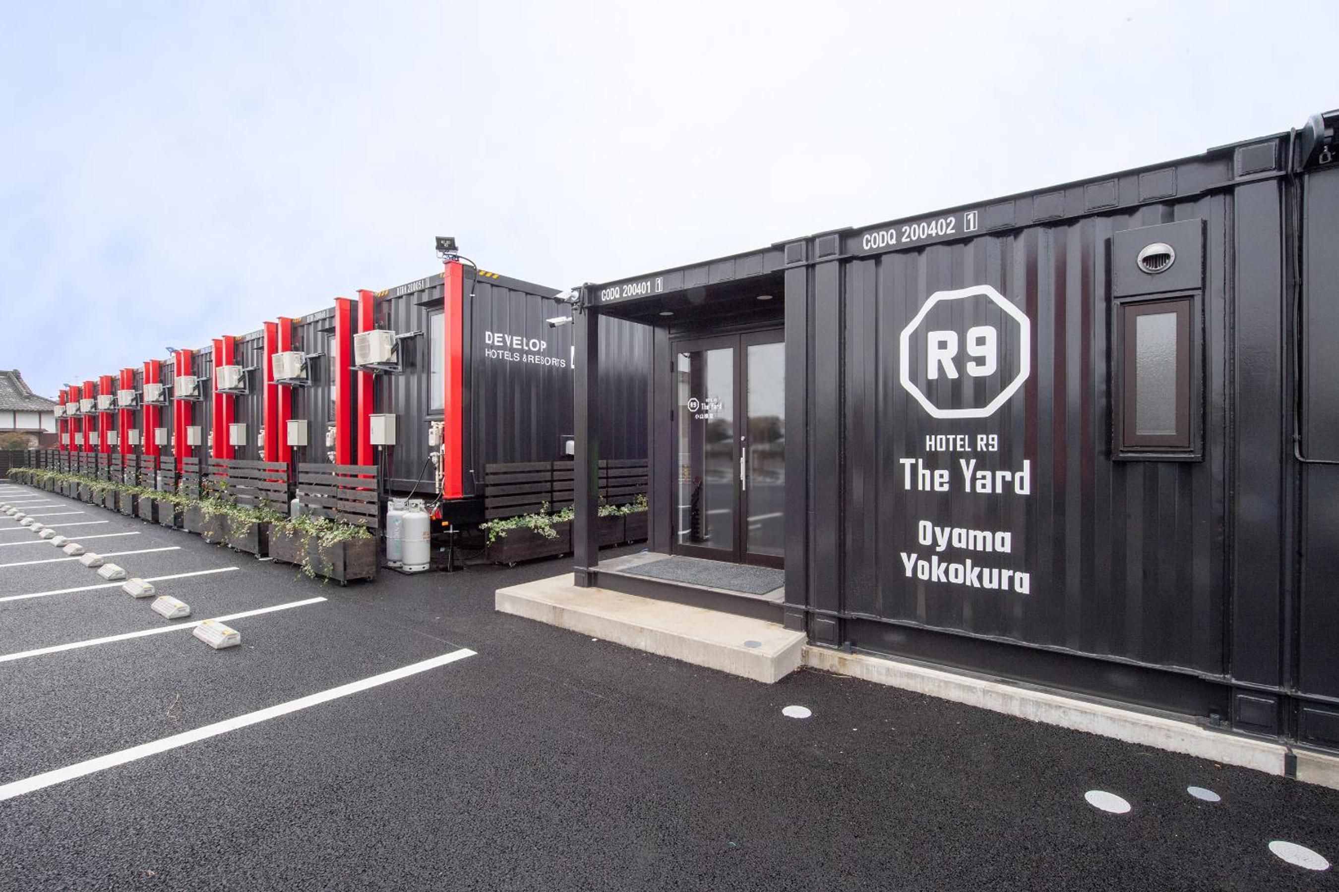 A row of black modular hotel units with red accents, each marked with a unique identifier, and a single unit labeled 'HOTEL R9 The Yard Oyama Yokokura.'