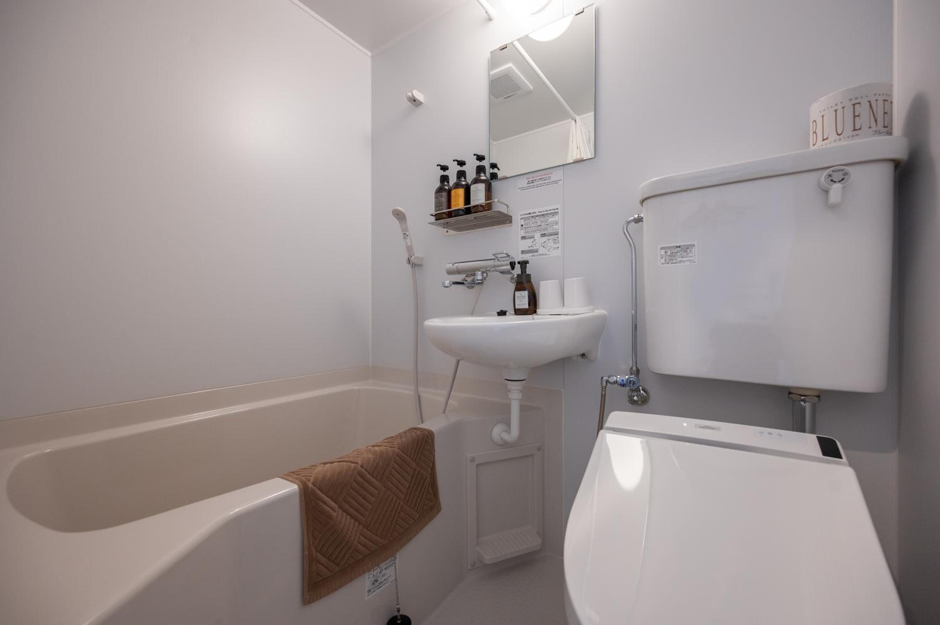 A bathroom with a bathtub, a sink, and a toilet. There are toiletries on a shelf above the sink.
