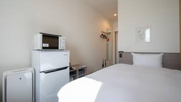 Quarto de hotel com cama, geladeira, micro-ondas e uma pequena mesa.