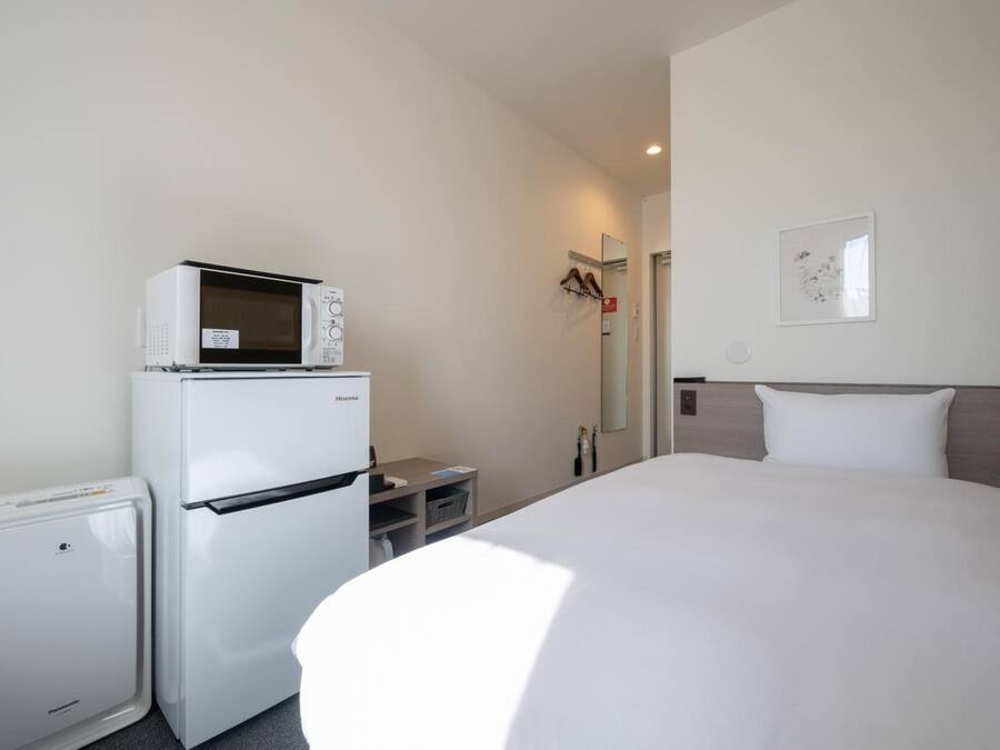 Quarto de hotel com cama, geladeira, micro-ondas e uma pequena mesa.