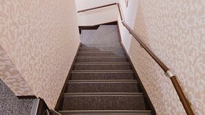 Una escalera con papel tapiz estampado en las paredes, barandilla y piso alfombrado.
