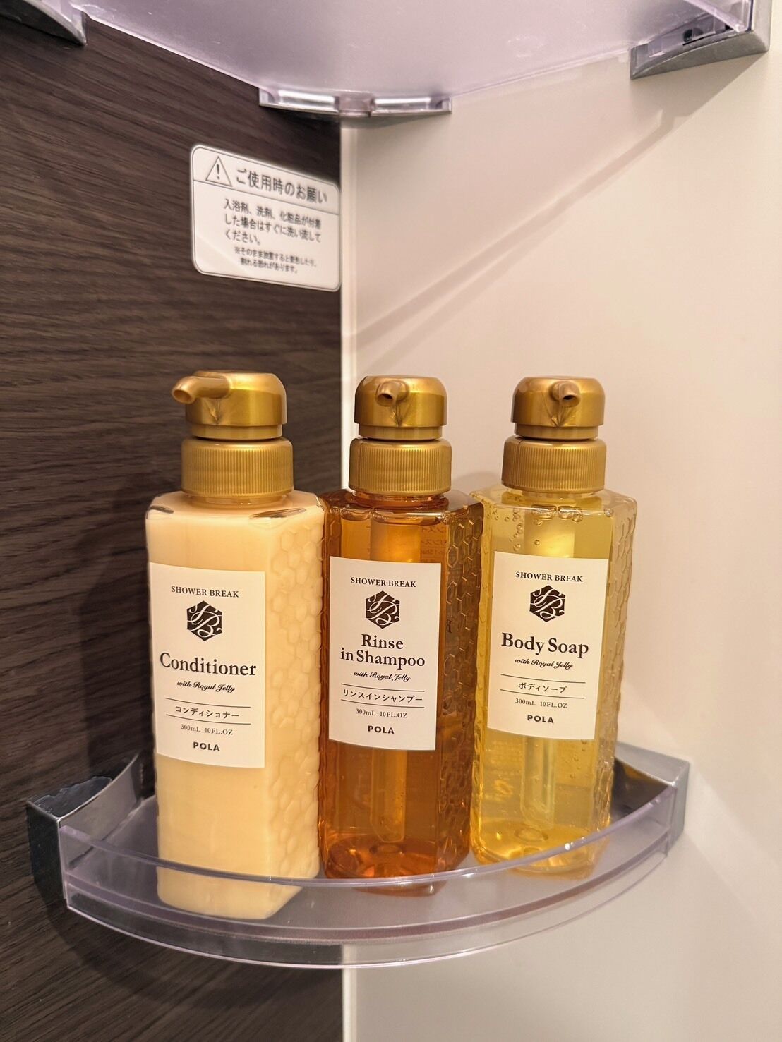 Three bottles of shower products on a transparent shelf in a bathroom.