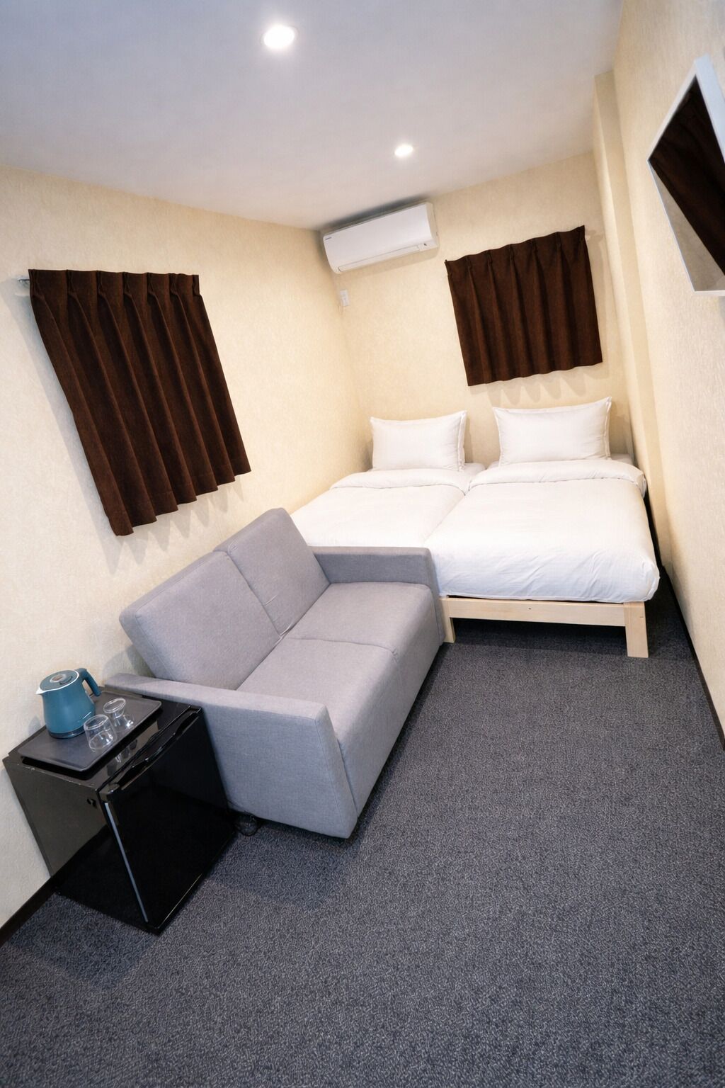 Habitación de hotel pequeña con cama, sofá, una mesita con un hervidor de agua y un equipo de aire acondicionado.
