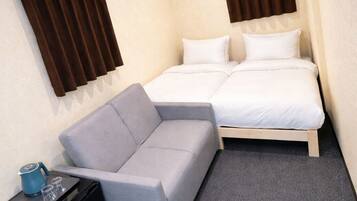 Habitación de hotel pequeña con cama, sofá, una mesita con un hervidor de agua y un equipo de aire acondicionado.