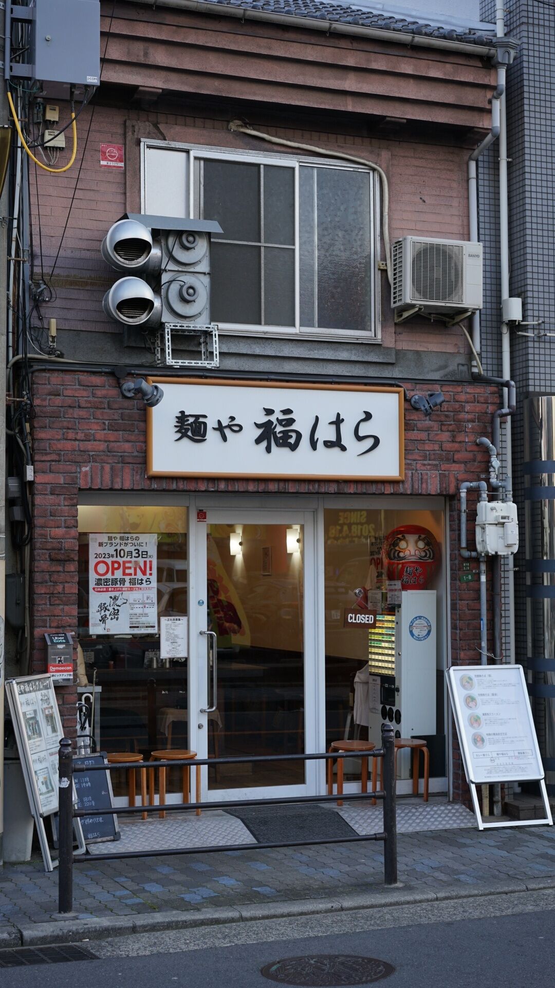 A storefront with a sign in Japanese, a closed sign, and a menu board outside.