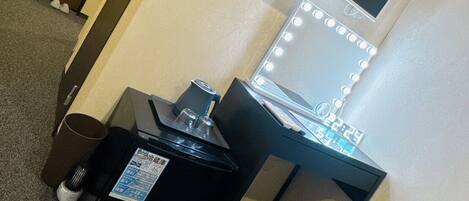 A hotel room with a desk, chair, and a vanity with lights.