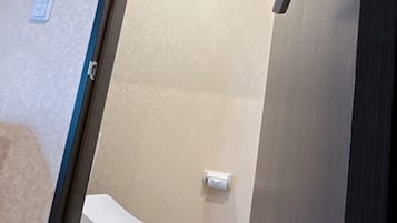 A small, narrow bathroom with a toilet, a towel dispenser, and a light fixture on the ceiling.