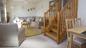 A cozy living room with a wooden staircase, a striped sofa, a wooden table, and a bookshelf. - Cottage in Jedburgh With Stunning Views (Jedburgh)