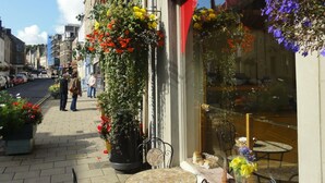 An outdoor café with tables and chairs, a flower arrangement, and a street view with pedestrians. - Cottage in Jedburgh With Stunning Views (Jedburgh)